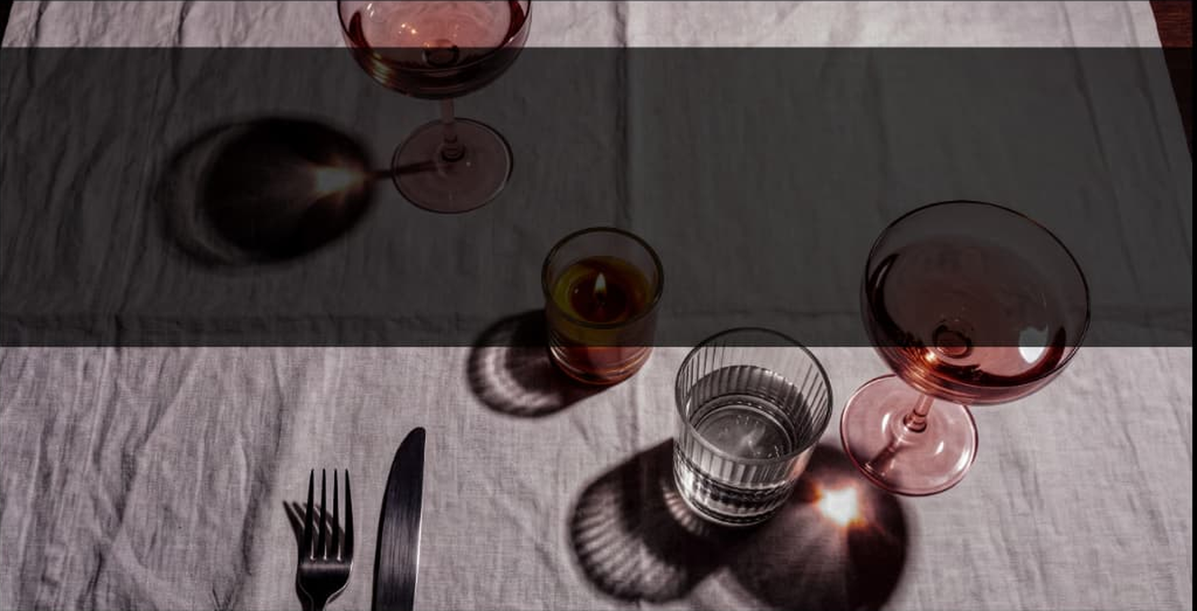 Wine glasses casting shadows across a white tablecloth